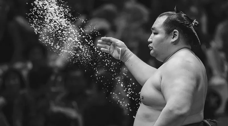 Black and white photo of a wrestler mid-salt-throw during a live tournament bout