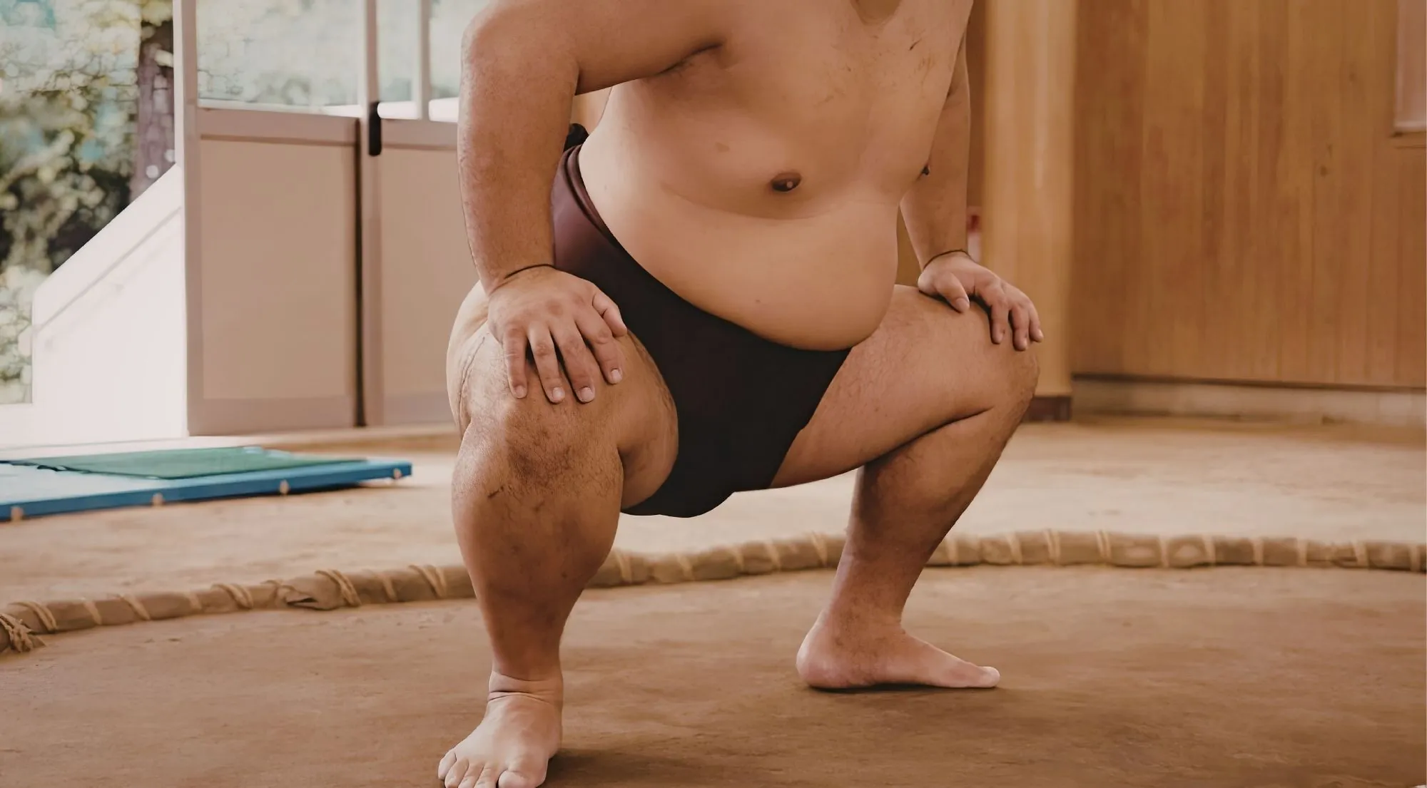 A single sumo wrestler crouched with hand on knee on a sand dohyo
