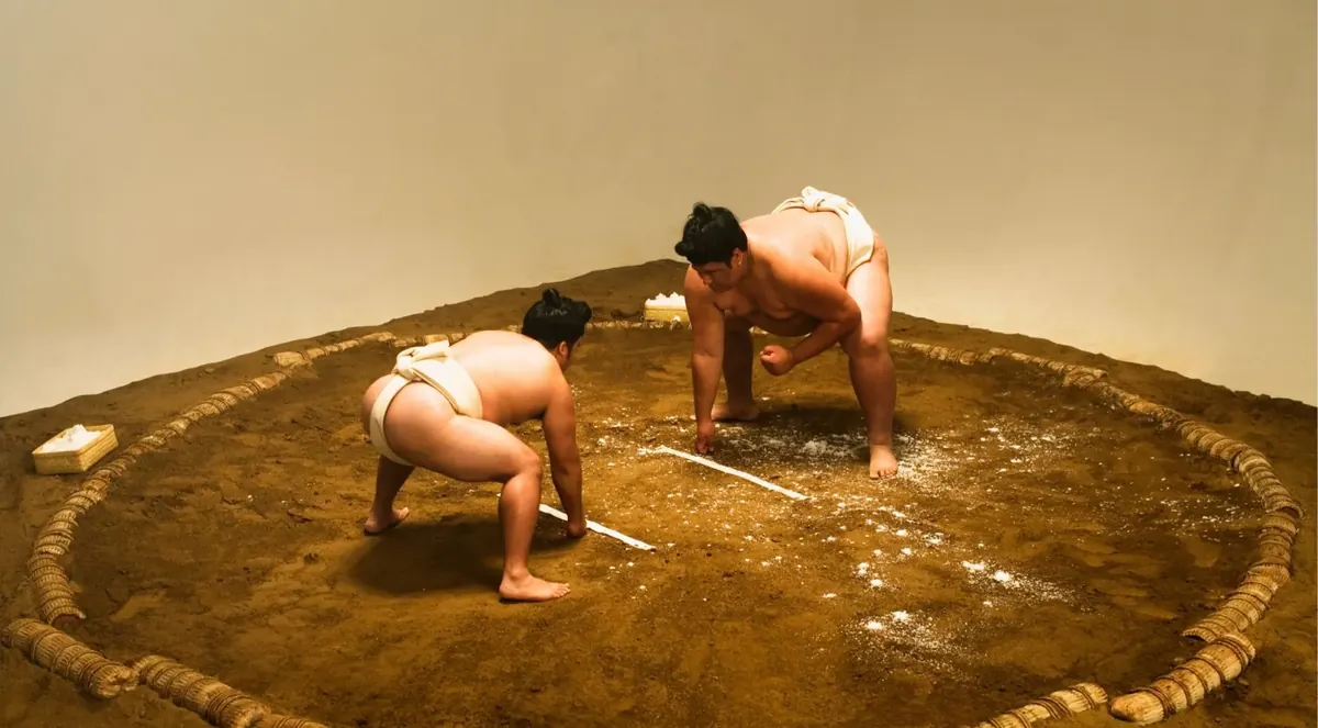 Two sumo wrestlers crouched facing each other on a clay ring before a bout