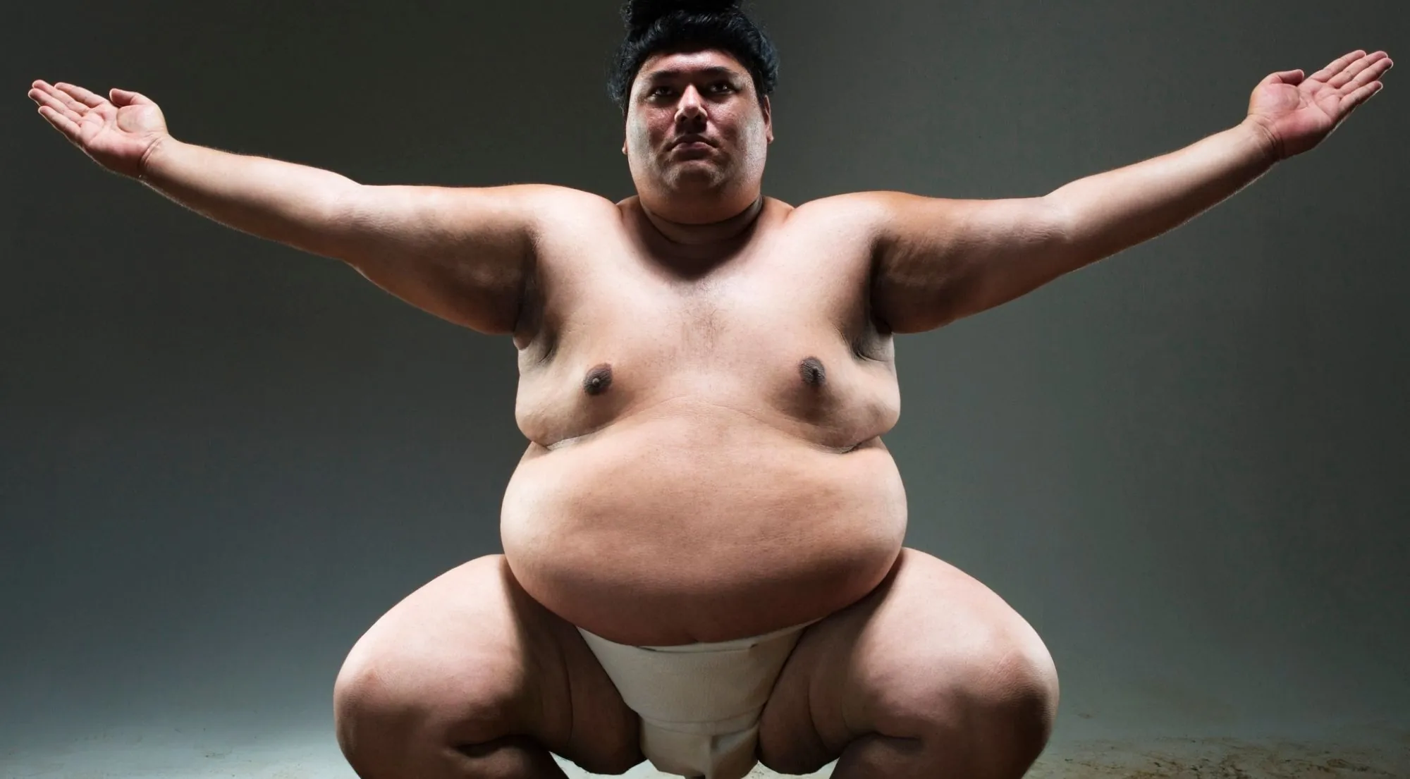 Studio portrait of a wrestler in the dohyo-iri ring-entering pose, arms outstretched